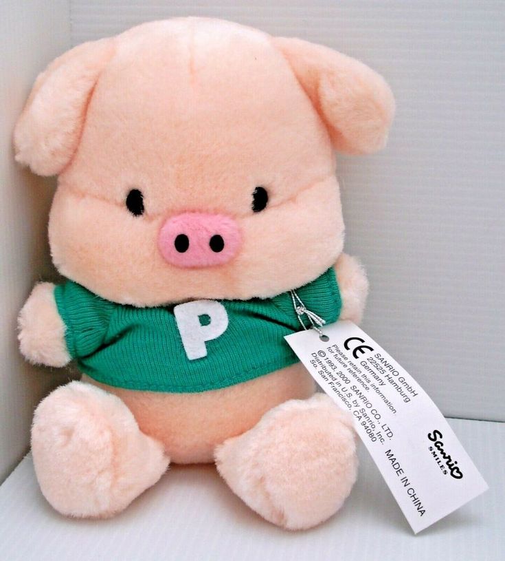 a pink stuffed pig with a green shirt on it's chest sitting next to a white wall