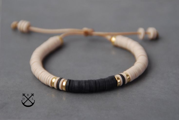 a white and black beaded bracelet on a gray surface with gold accents, sitting next to a string