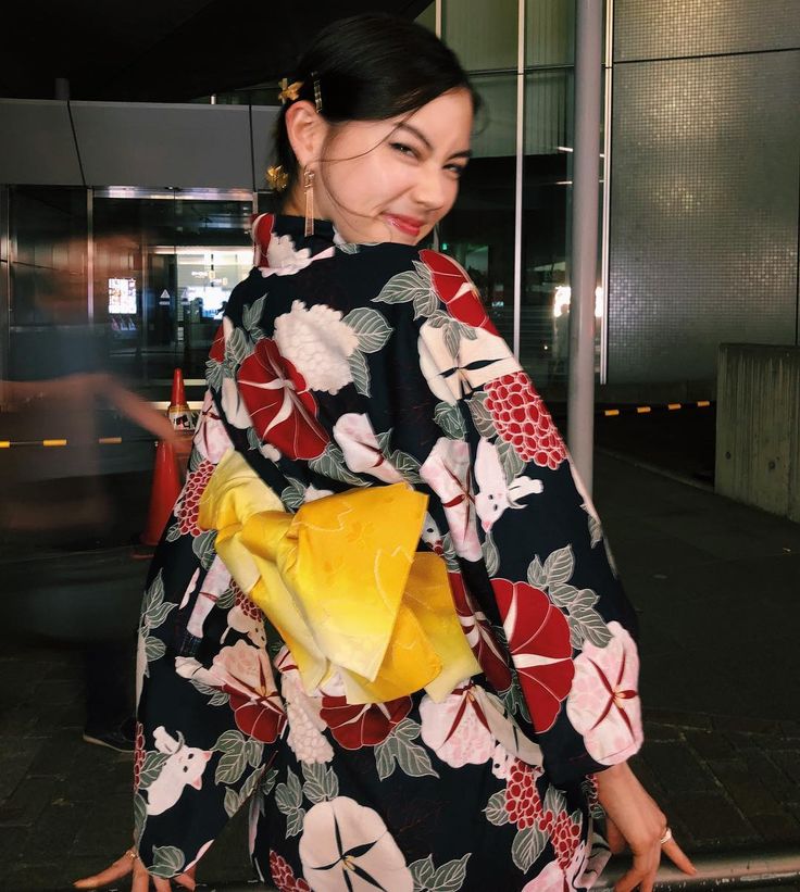 a woman in a black and yellow kimono is walking down the street with her hand on her hip