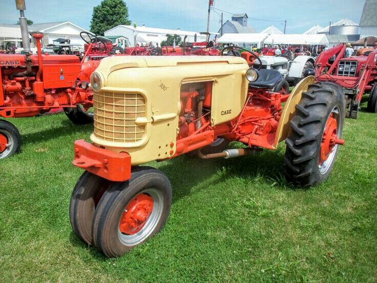 an old yellow tractor parked on top of a lush green field next to other red and white tractors