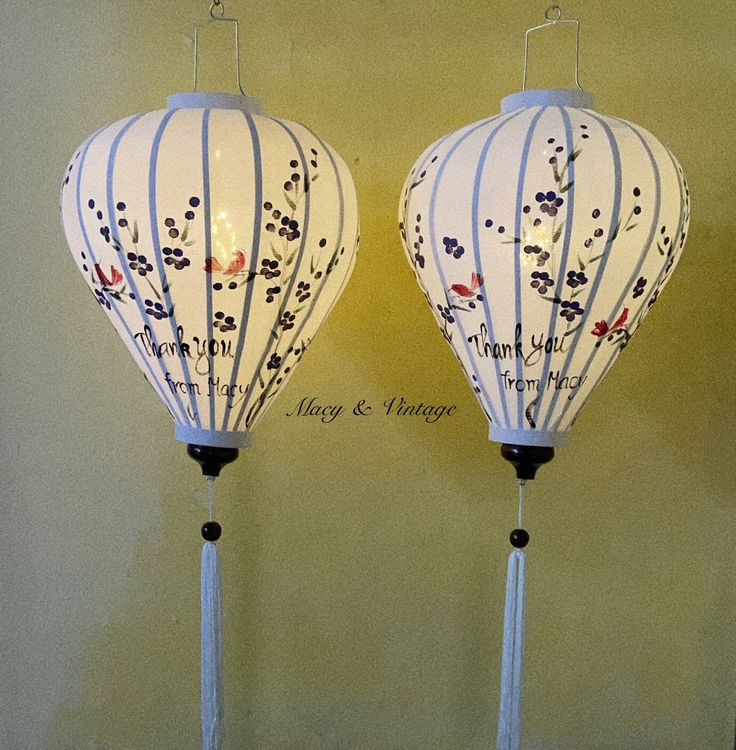 two white lanterns with designs on them sitting next to each other in front of a yellow wall