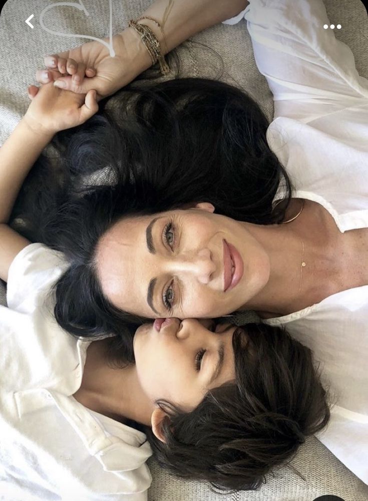 two women laying on top of a bed next to each other with their arms around one another