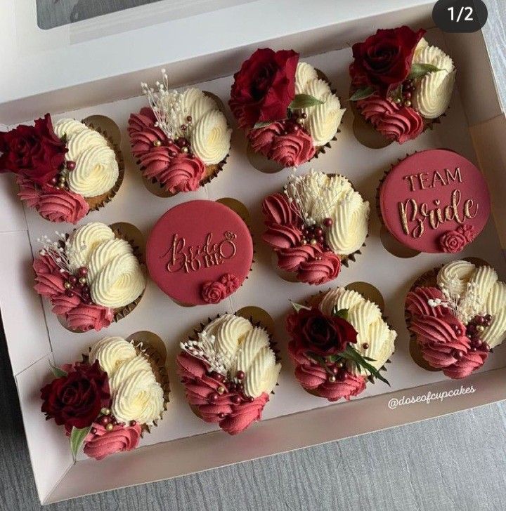 twelve cupcakes in a box decorated with red and white frosting, roses and the words team bride