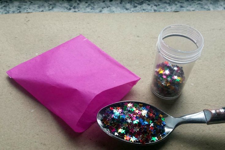 a spoon with some glitter on it next to a pink paper bag and a pair of scissors