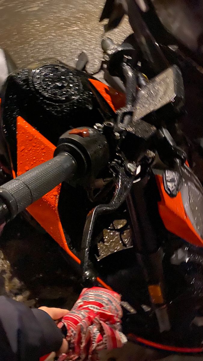 an orange and black motorcycle being worked on by a person in the water with a hose attached to it