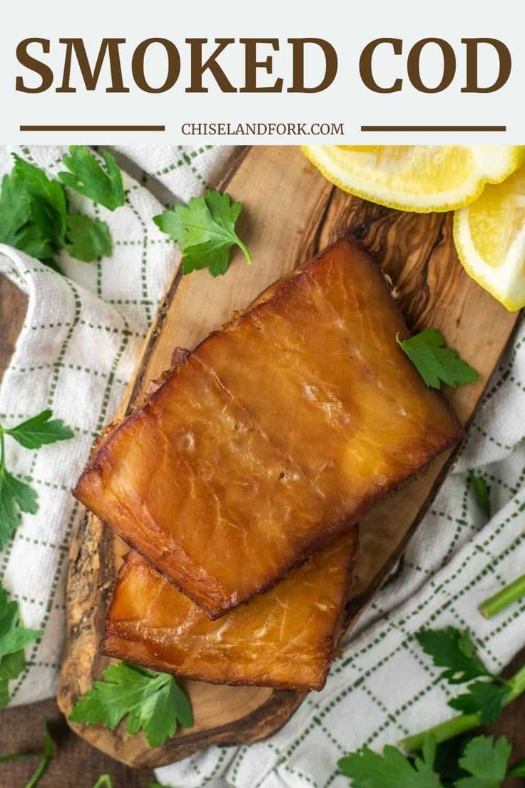 two pieces of fish sitting on top of a cutting board next to lemons and parsley