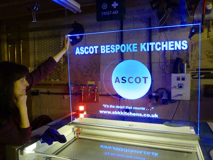 a woman standing in front of a neon sign that reads ascott bespoke kitchens