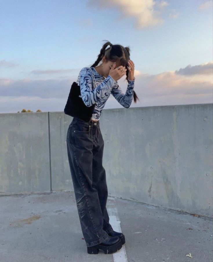 a woman standing on top of a cement wall with her hands to her face while covering her eyes