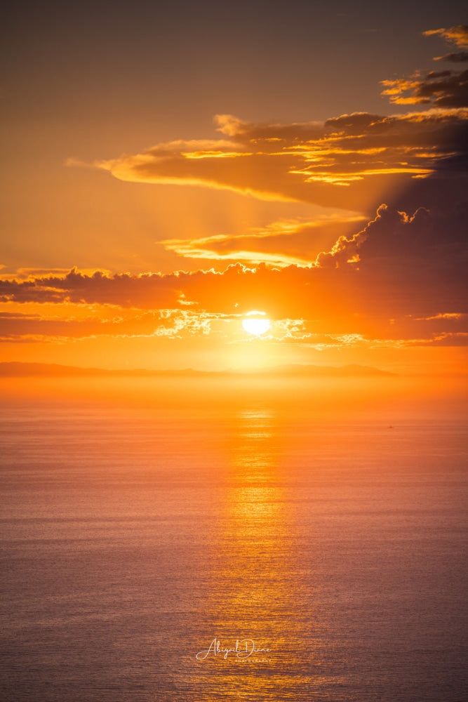 the sun is setting over the ocean with clouds in the sky and water below it