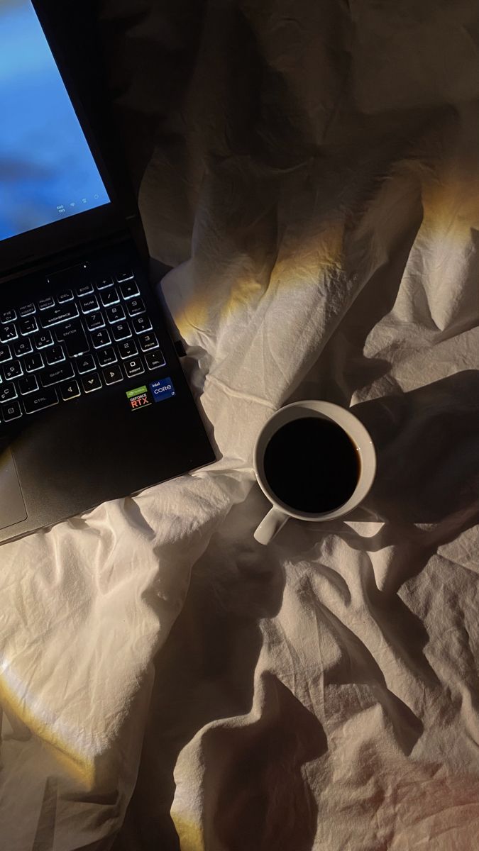 a laptop computer sitting on top of a bed next to a cup of black coffee