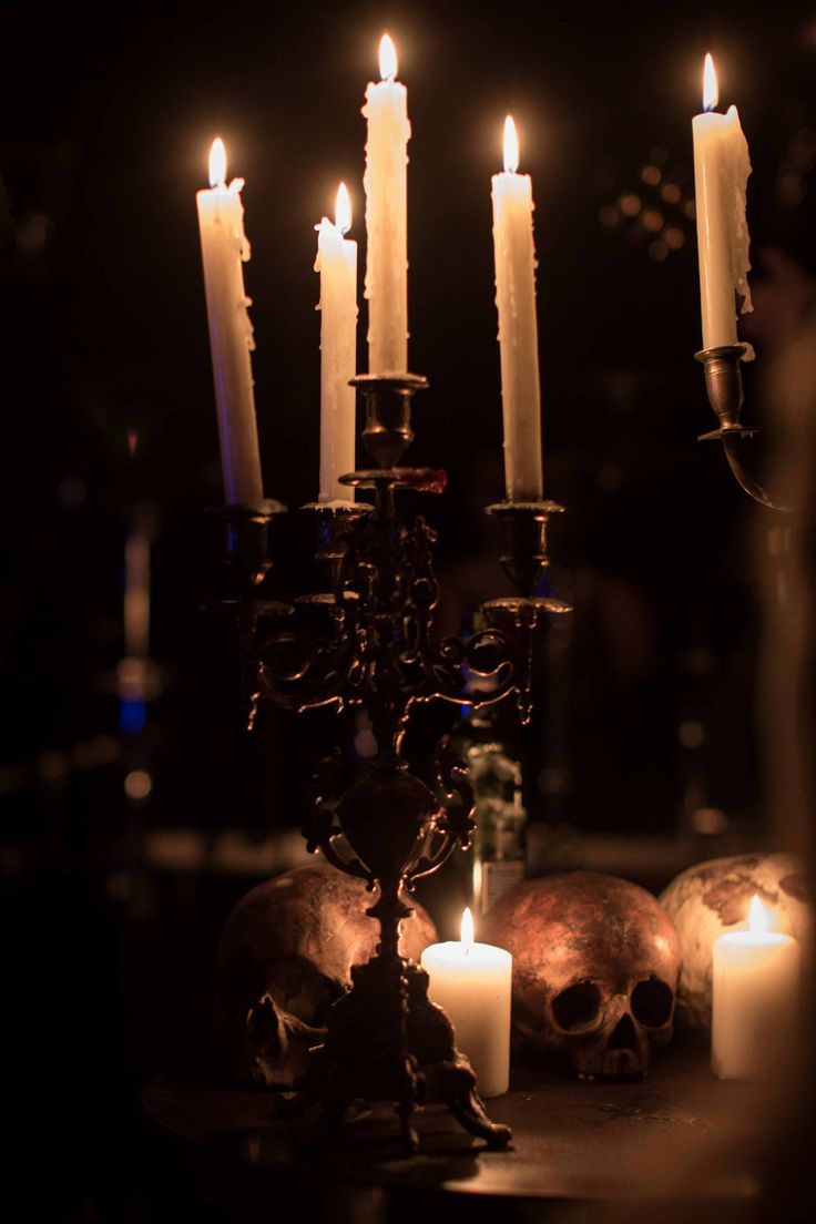 there are many candles that are lit in the dark room with skulls on the table