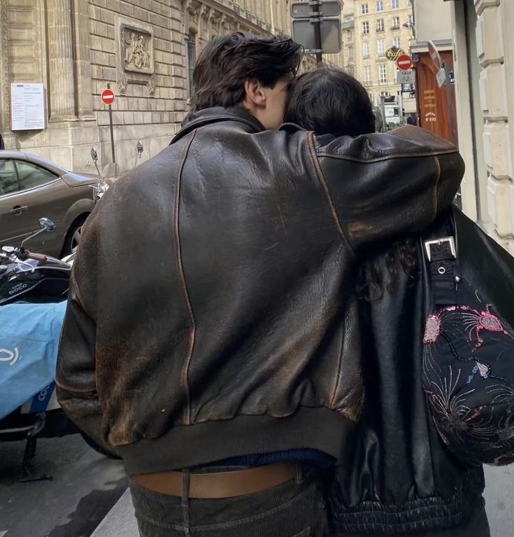 two people walking down the street with their backs to each other and one person wearing a leather jacket