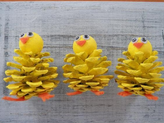 three yellow pine cones with faces made to look like birds sitting on top of them