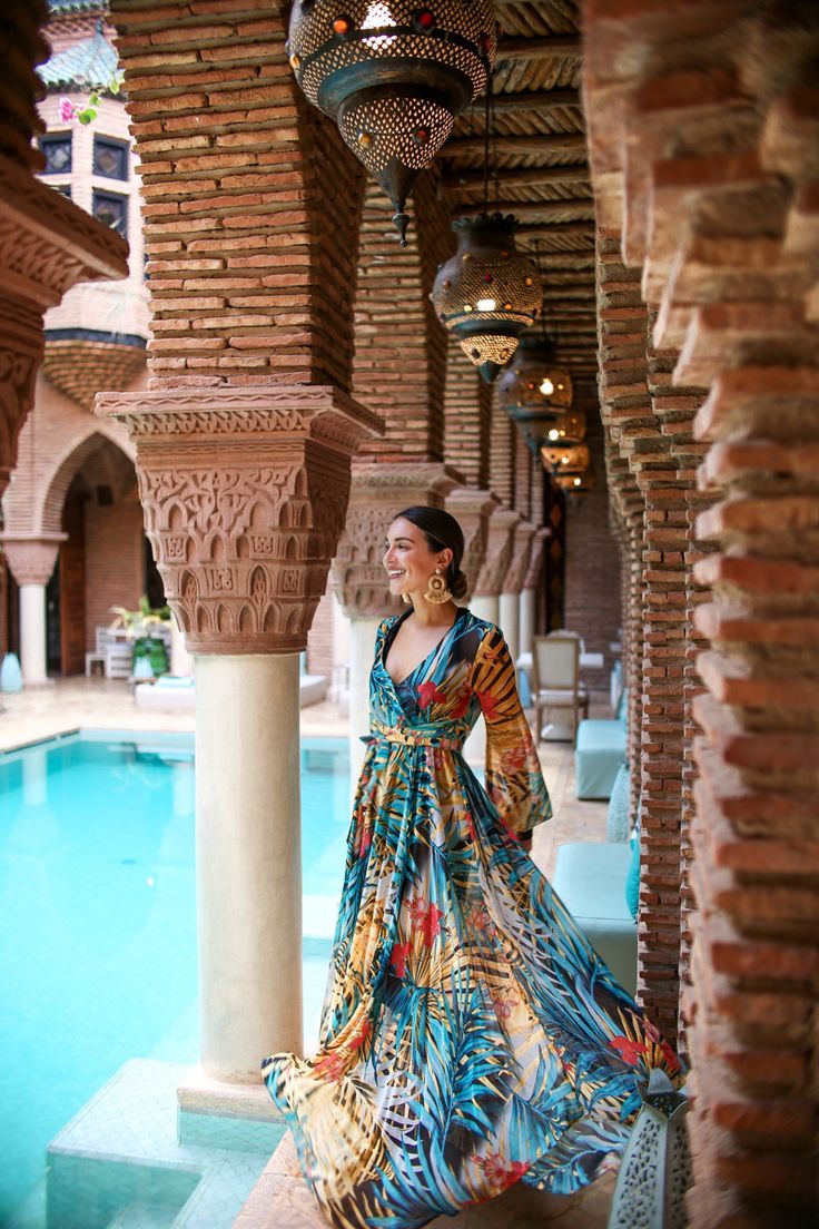 a woman standing next to a pool wearing a colorful dress