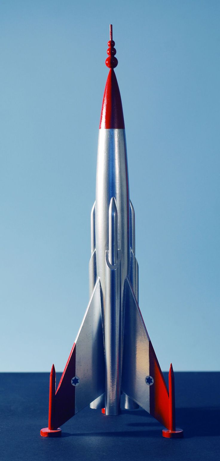 a silver and red rocket ship sitting on top of a blue surface with no clouds in the background