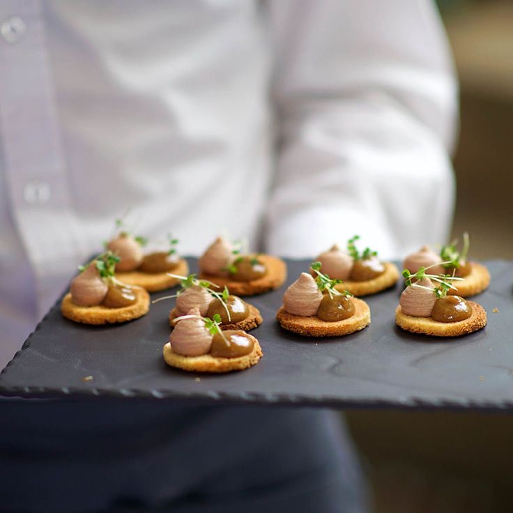 small crackers topped with peanut butter and sprouts on a black platter