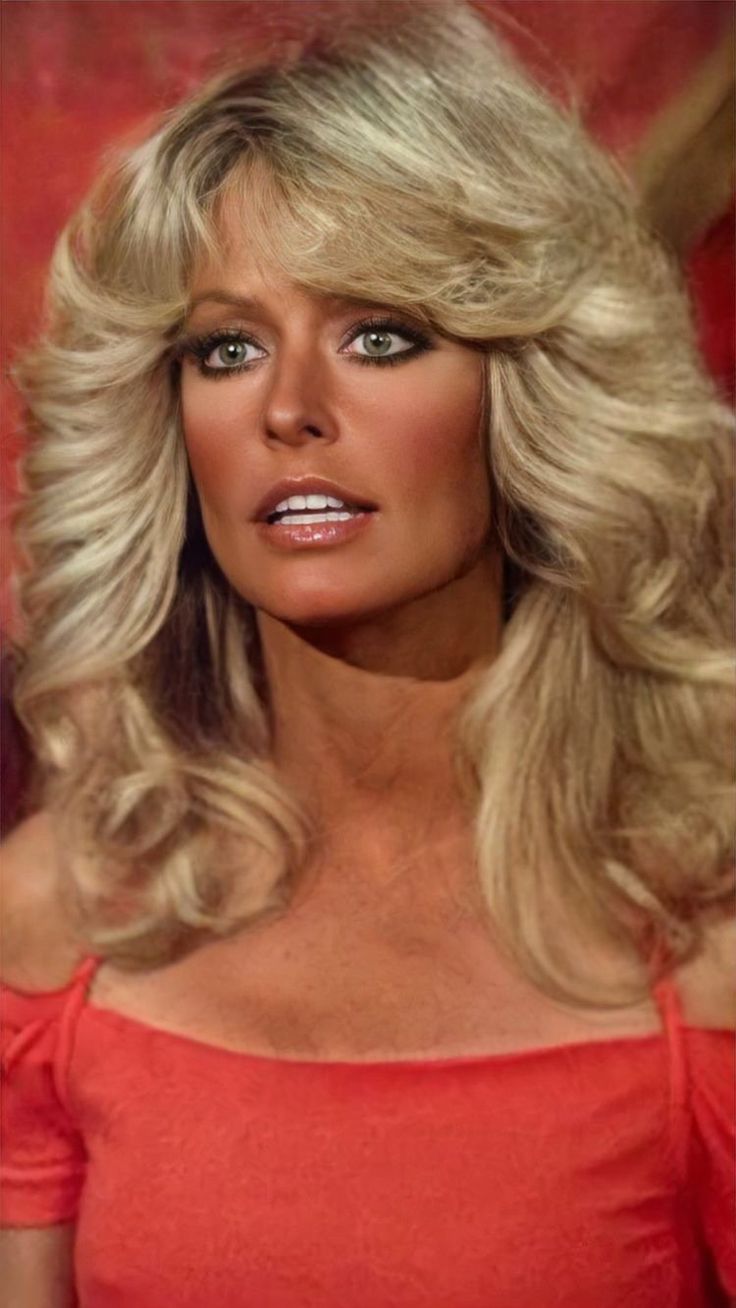 a woman with long blonde hair wearing an off the shoulder red top and looking to her left