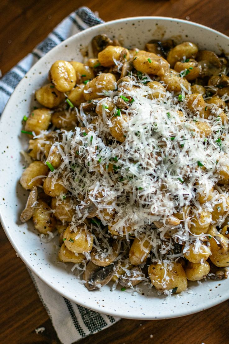 a white bowl filled with pasta covered in parmesan cheese on top of a wooden table