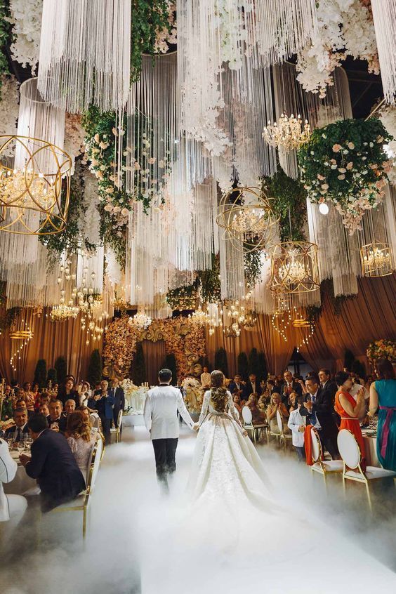 a wedding ceremony with chandeliers hanging from the ceiling and people walking down the aisle