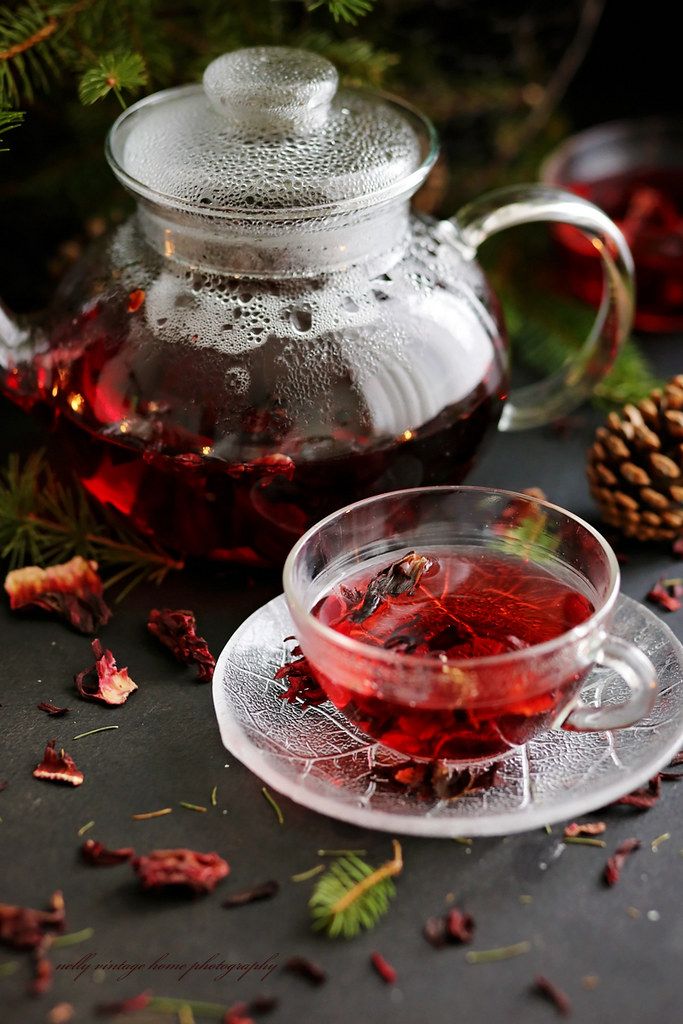 a glass tea pot filled with red liquid next to a cup and saucer on a table