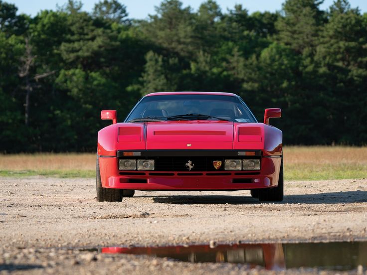 a red sports car parked on the side of a dirt road next to a forest