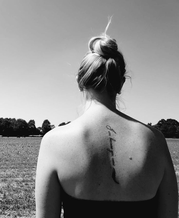 a woman with a tattoo on her back stands in a field and looks at the sky