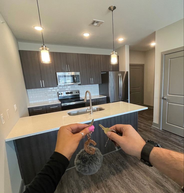 two hands holding scissors in front of a kitchen island with an island countertop and stainless steel appliances