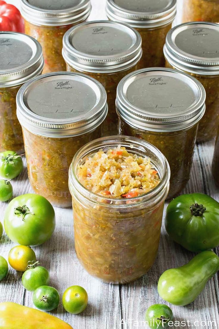 several jars filled with food sitting on top of a table next to green peppers and tomatoes