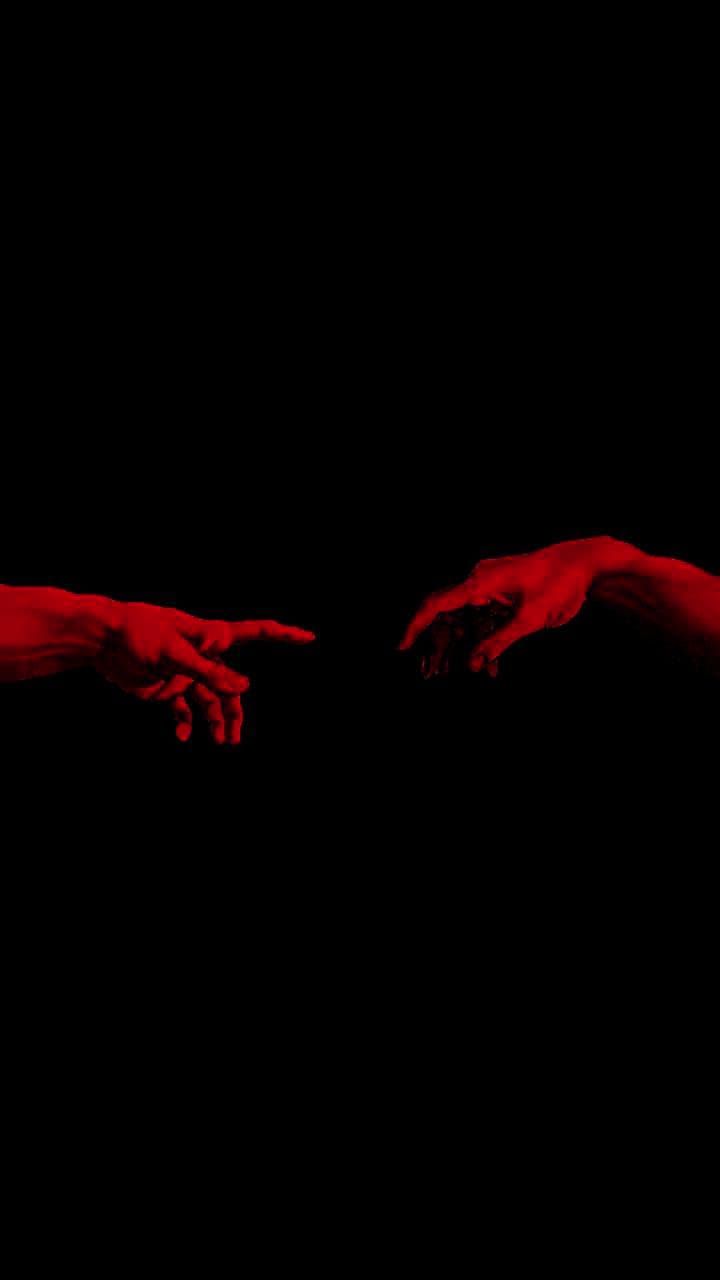 two hands reaching towards each other with red paint on their fingertipss in the dark