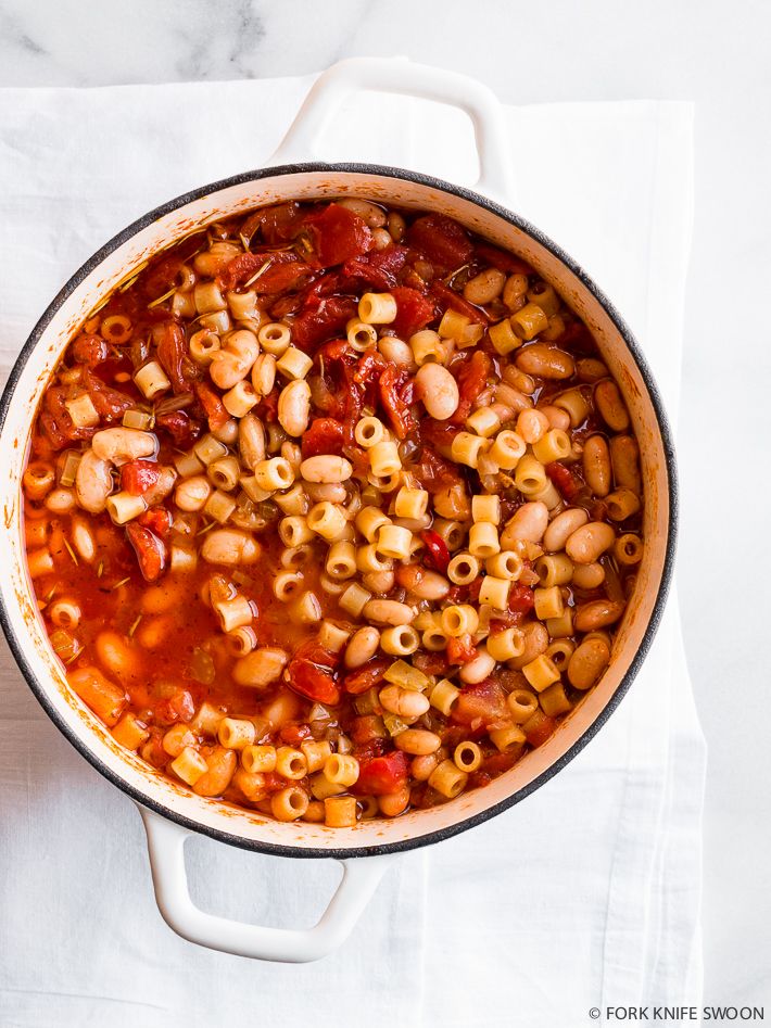 a pot filled with pasta and sauce on top of a white cloth next to a wooden spoon