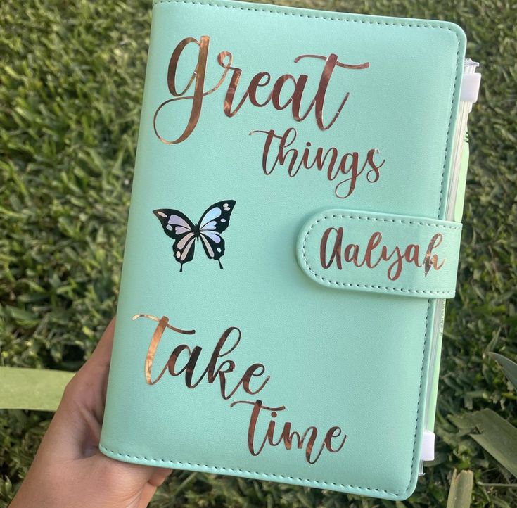 a hand holding up a notebook with writing on it and a butterfly attached to the cover