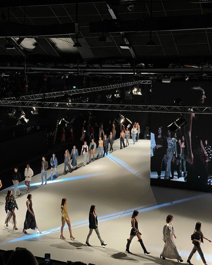 many people are walking down the runway at a fashion show in front of a large screen