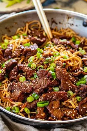 beef and noodles in a skillet with chopsticks on the side, ready to be eaten