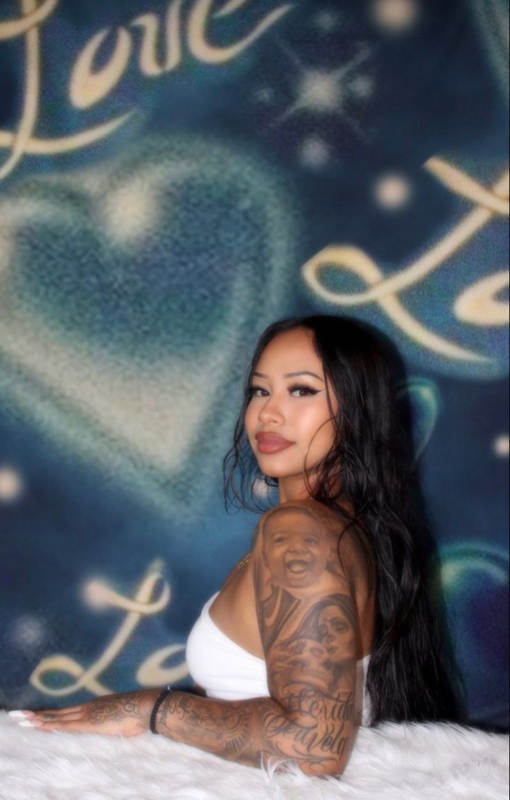 a woman with tattoos on her arms and chest sitting in front of a backdrop that says love you