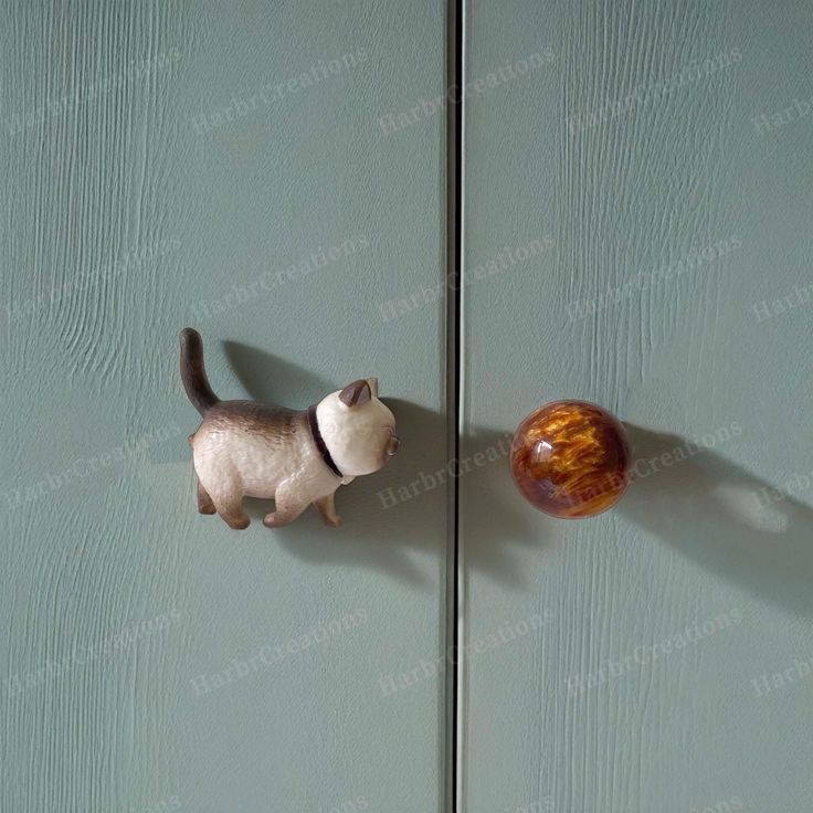 a cat figurine standing next to an apple on a green door with shadow