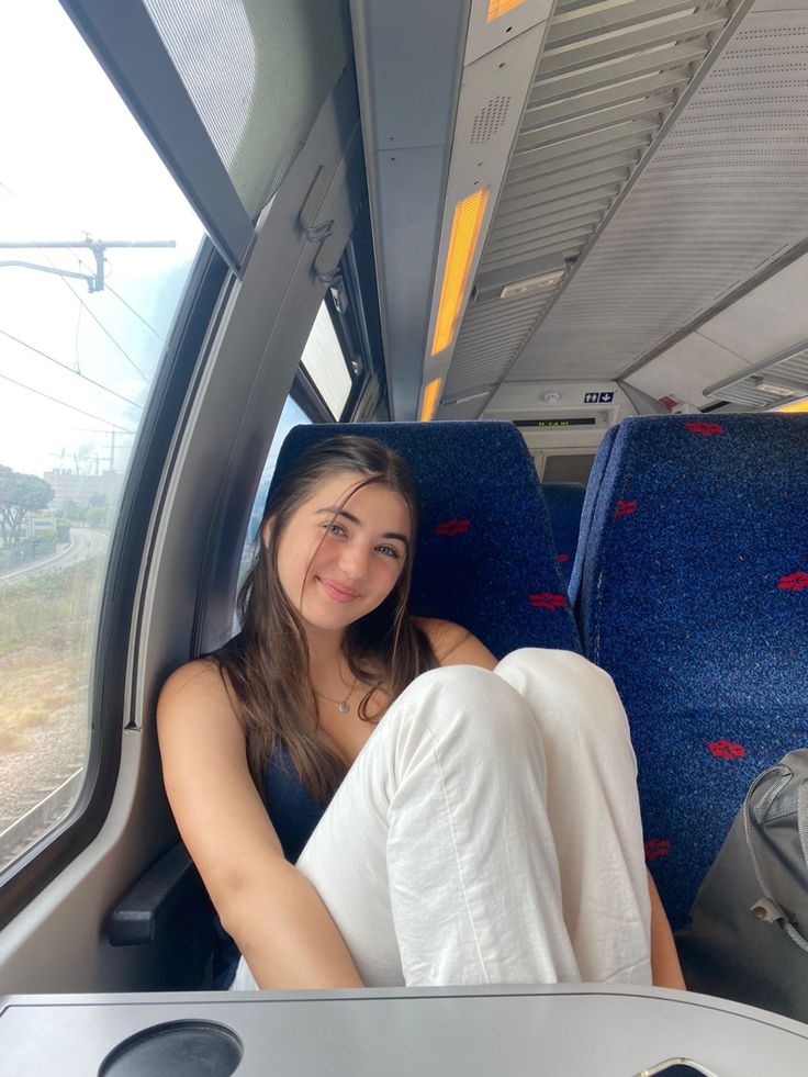 a woman sitting in the back of a bus with her legs crossed and looking at the camera