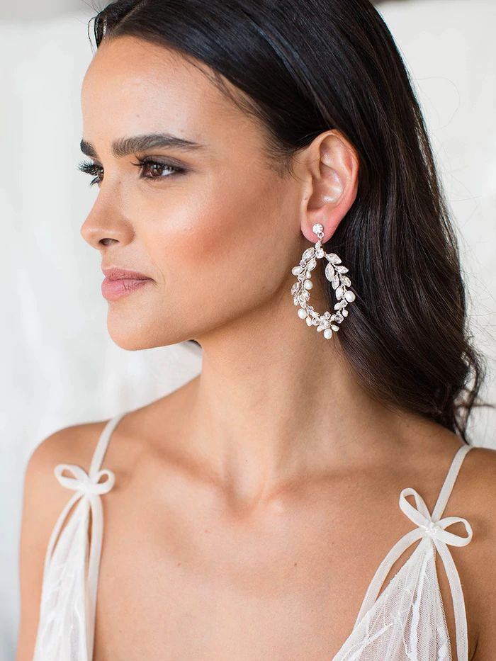 a woman in a white dress wearing large earrings with bowknots on them