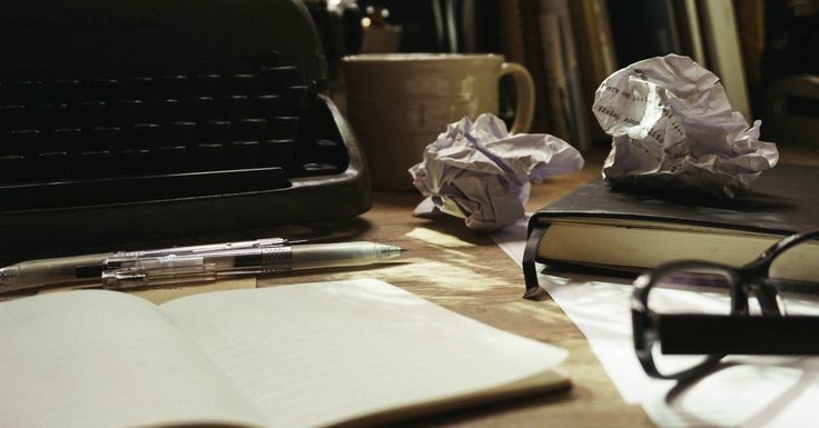 an open book sitting on top of a wooden table next to glasses and a typewriter