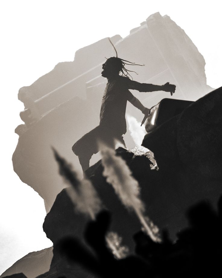 a man with dreadlocks standing on top of a rock in front of a mountain