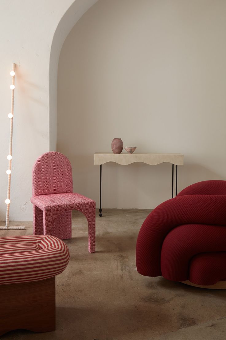 two chairs and a table in a room with white walls, one pink chair and the other red