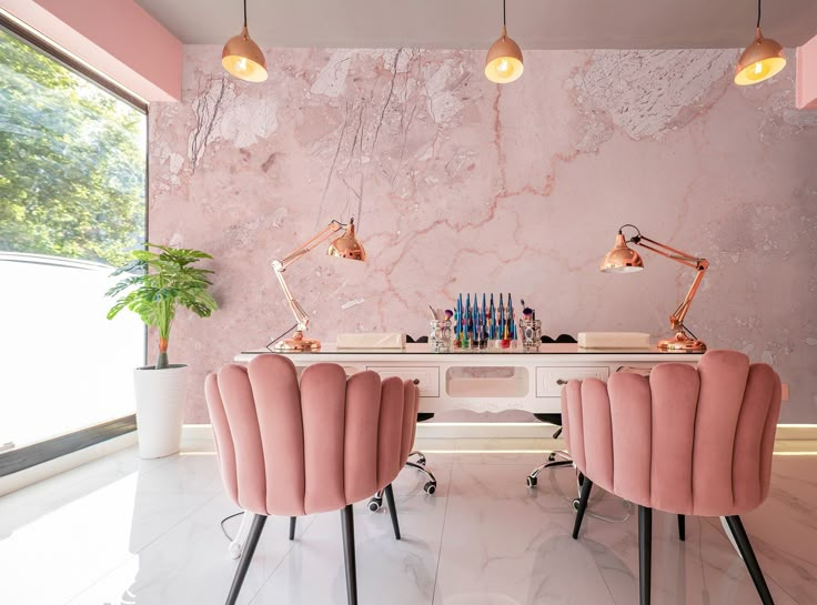 two pink chairs sitting next to each other in front of a desk with lights on it