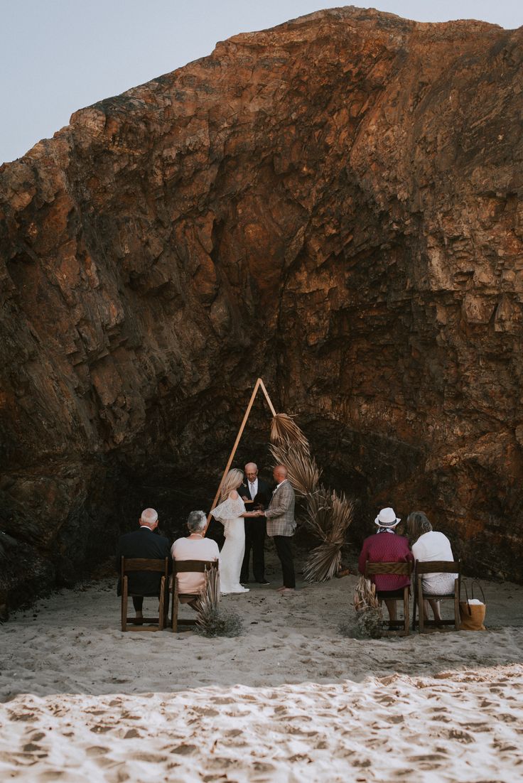 a group of people sitting on top of a sandy beach next to a large rock