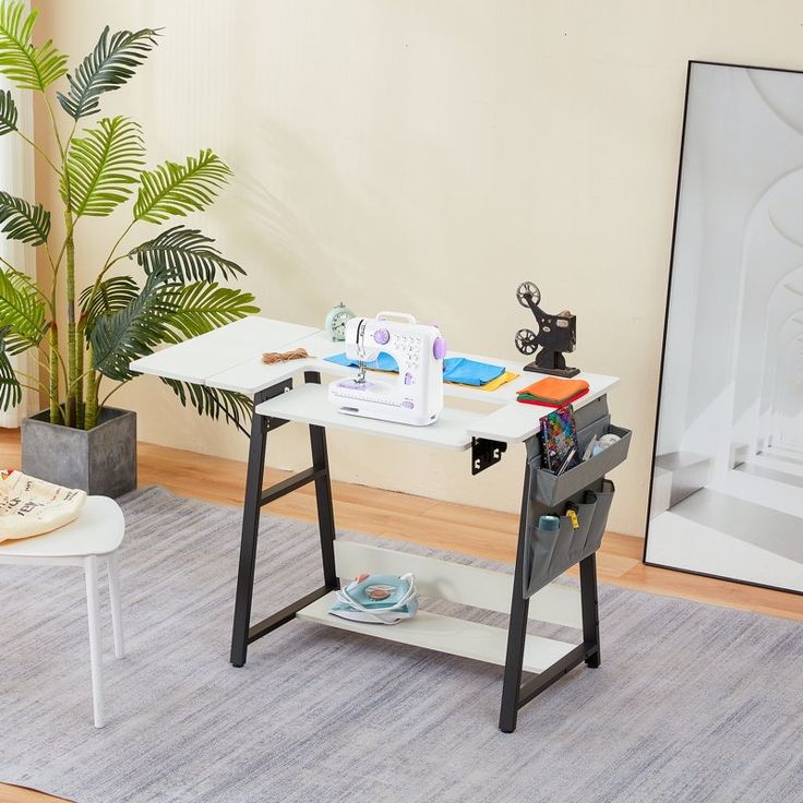 a table with sewing supplies on it next to a potted plant in a living room