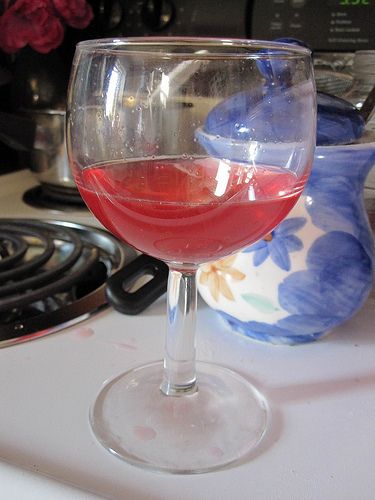 a glass of red wine sitting on top of a counter next to a pot and pan