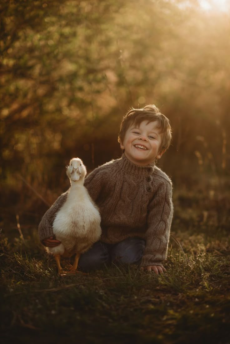 a little boy sitting on the ground with a duck in his lap and smiling at the camera