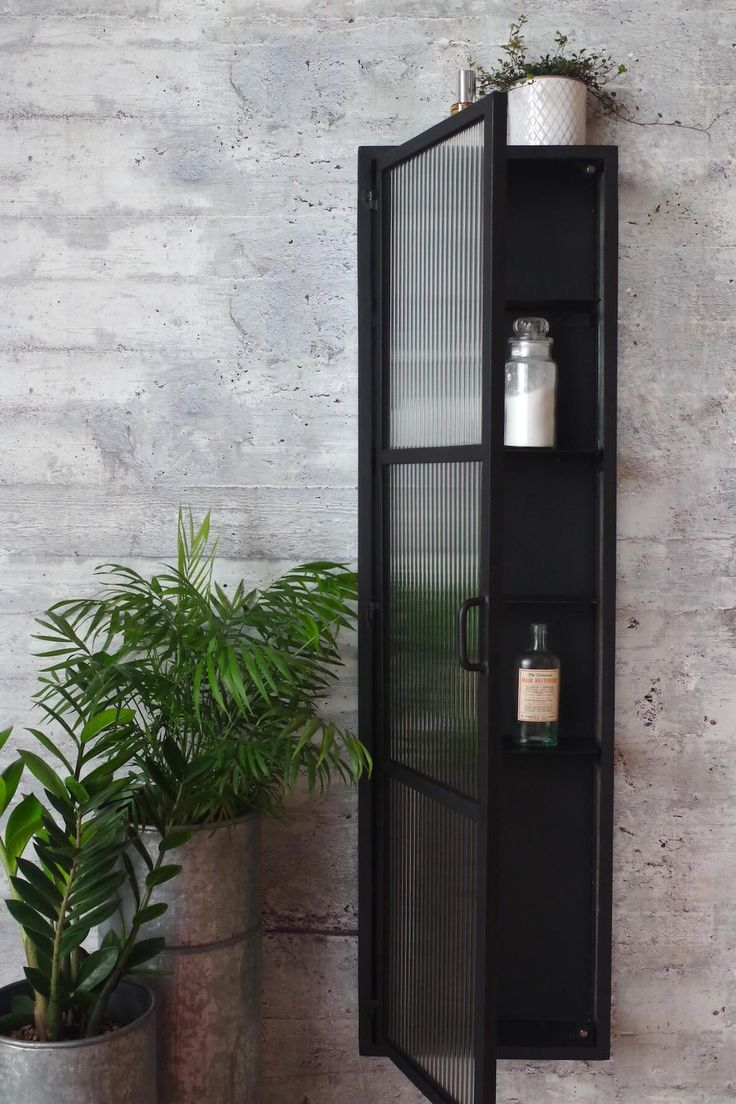 a tall black cabinet next to a potted plant and a wall mounted candle holder