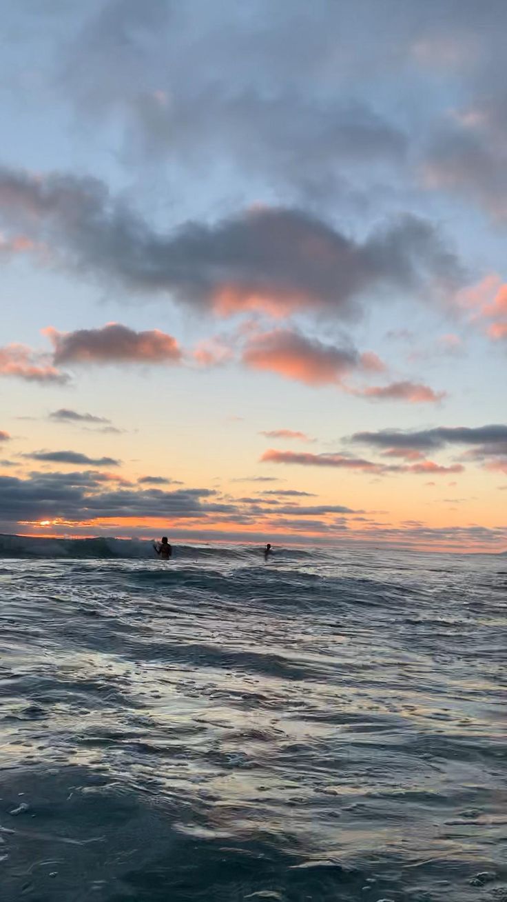 two surfers are riding the waves in the ocean at sunset or dawn with clouds above them