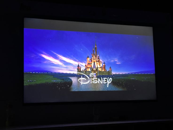 the disney logo is projected on a screen in front of a dark background with blue sky and clouds