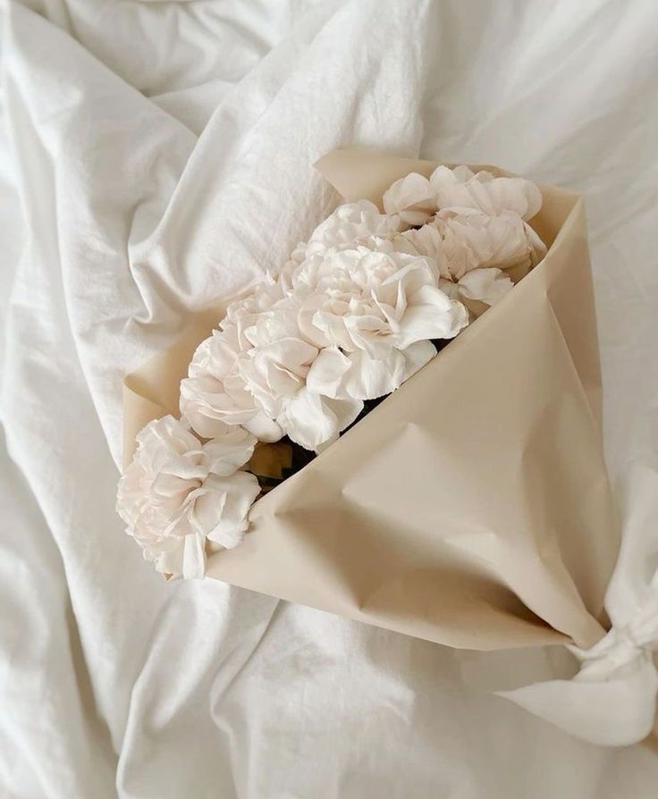 a bouquet of flowers is wrapped in a white sheet on a bed with sheets and pillows