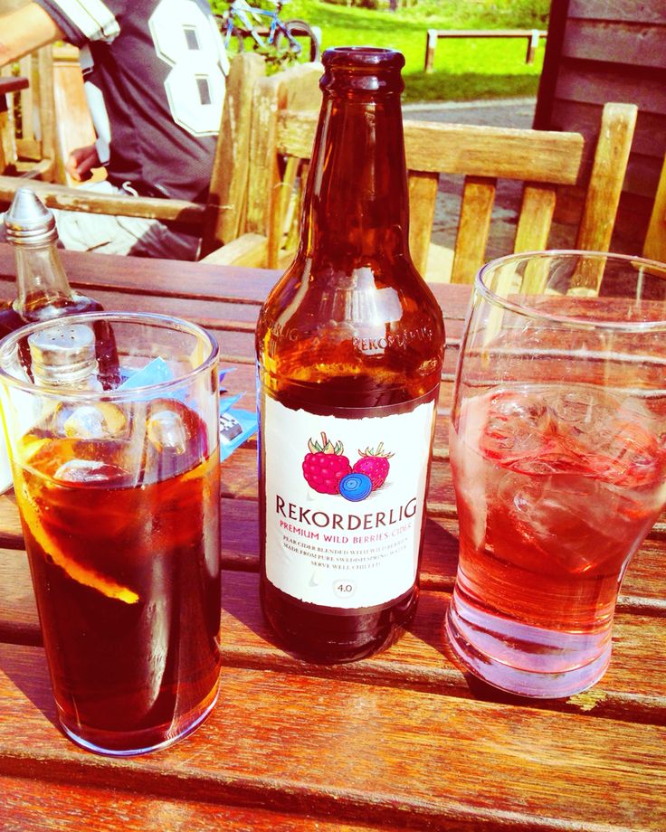 two glasses and a bottle sitting on a wooden table with drinks in front of them